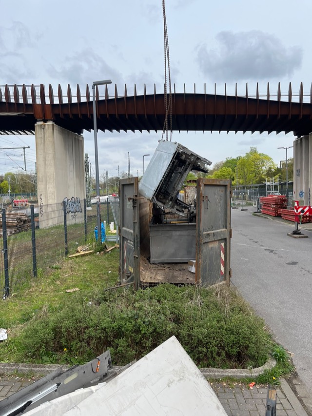 Ausgebautes Anlagenteil hängt am Kranhaken über einem Abfallcontainer